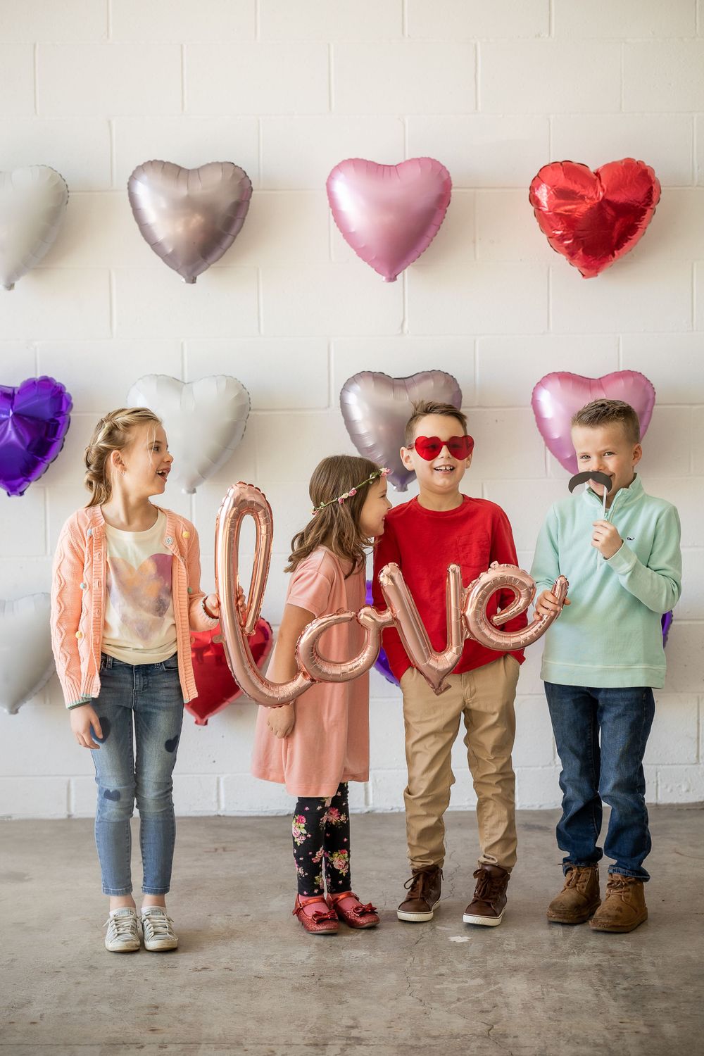 Heart-shaped balloons in silver, pink and red decorate a white wall for a Valentine's celebration.