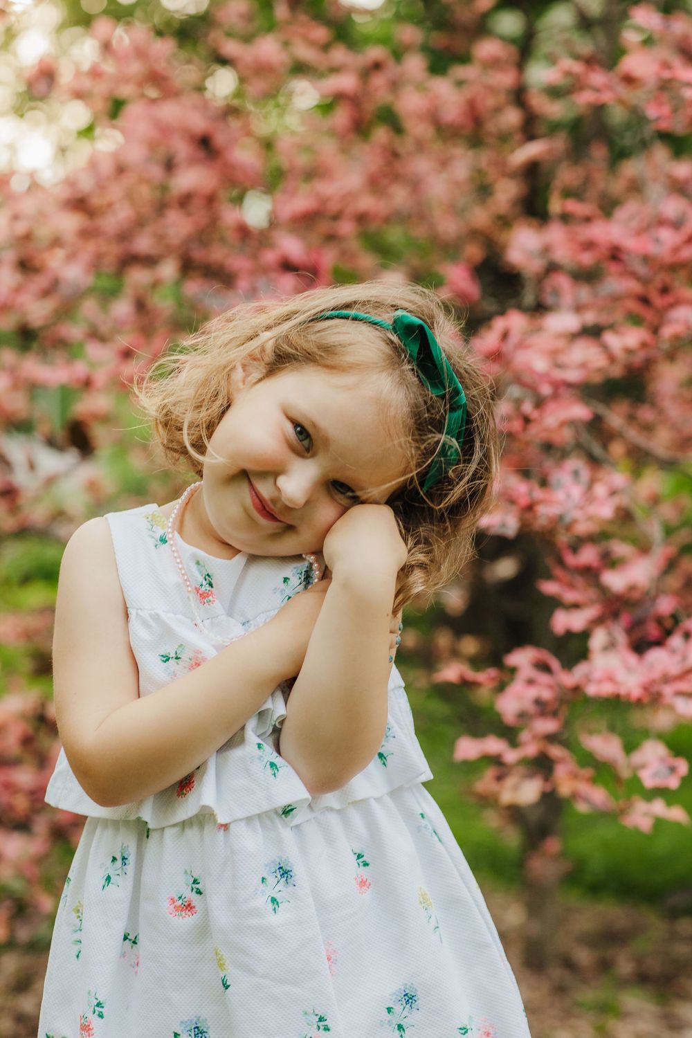 Sweet moment captured as child poses playfully against blooming pink spring trees.