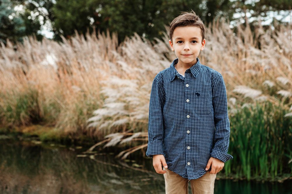Child in blue plaid shirt standing near a pond with pampas grass in the background.