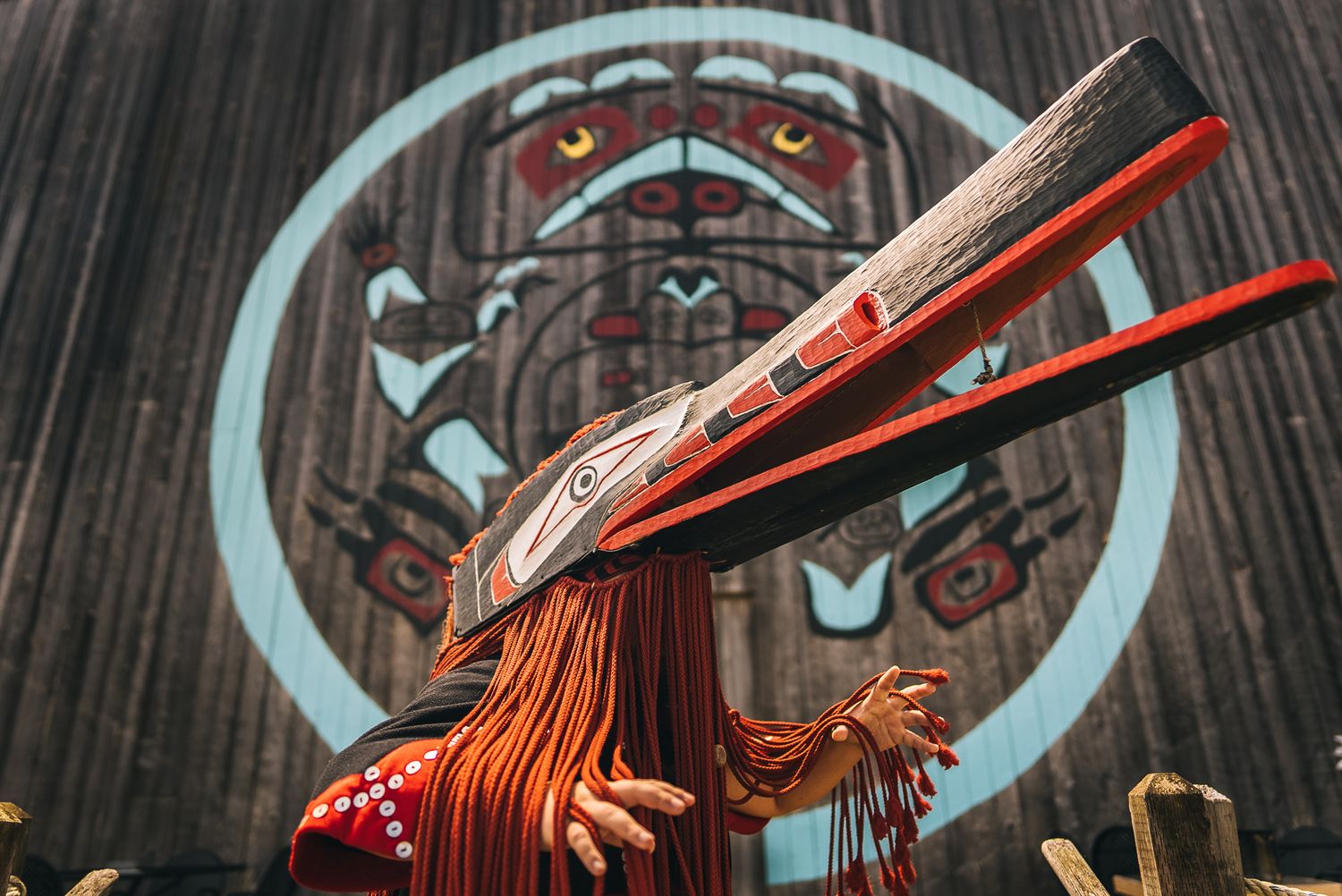 Traditional Native American ceremonial headdress with red feathers against tribal artwork background.