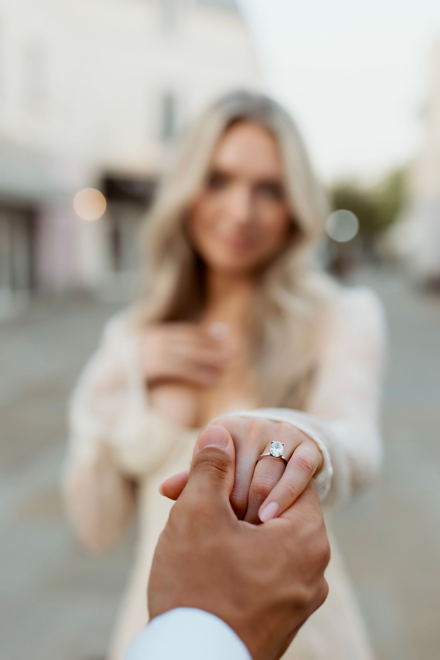 Close-up of an engagement ring being shown on a woman's finger with a blurred background.