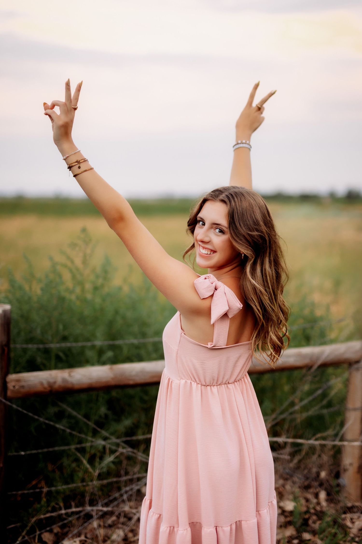 Woman in flowing pink dress makes peace signs while posing in rural setting in Milton, FL