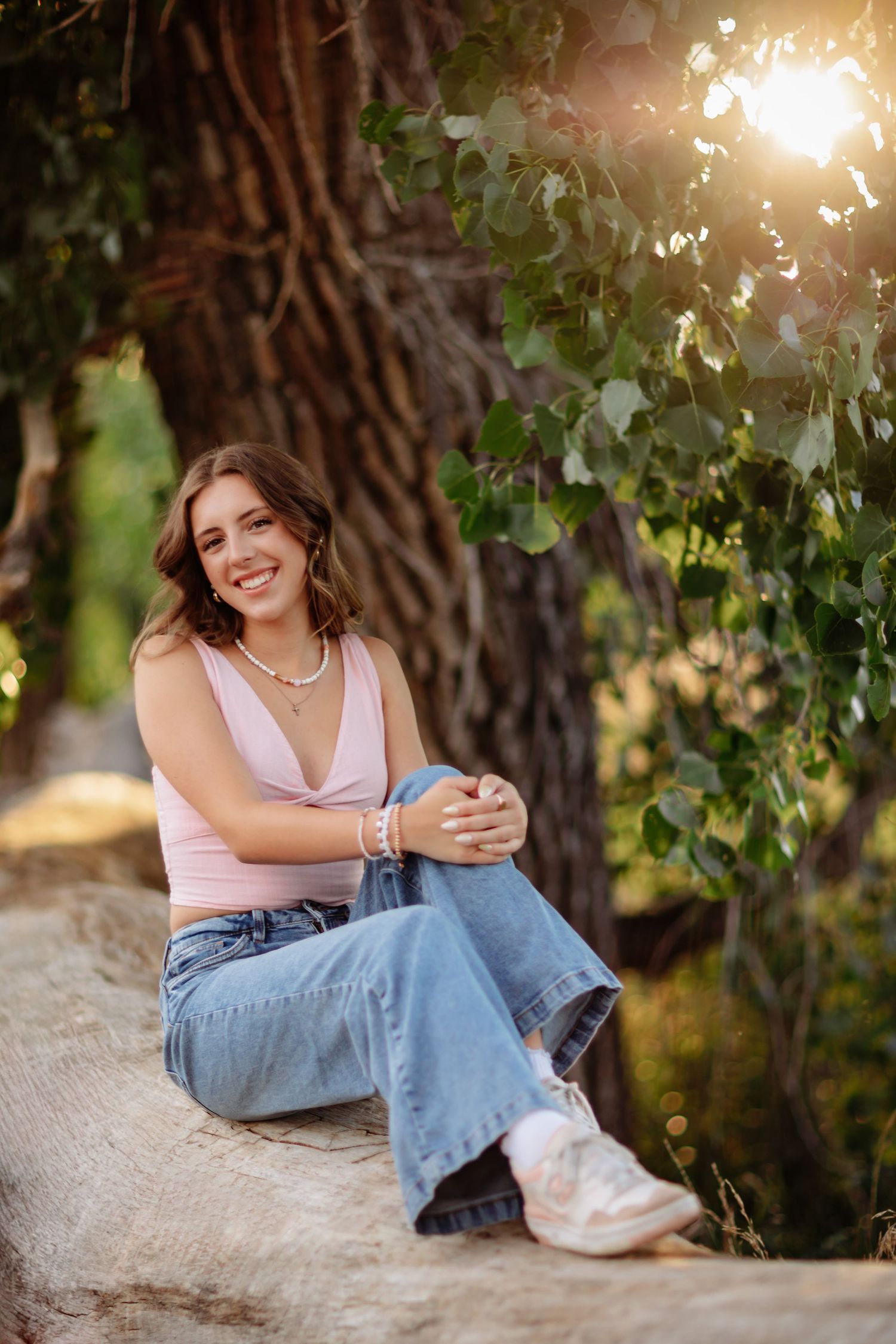 Woman in pink tank top and jeans sits relaxed by tree during sunset photoshoot in Milton FL