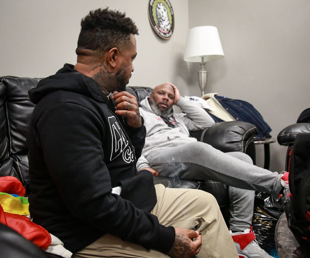 Two professional athletes prepare in a locker room with white walls and soft lighting before a game.