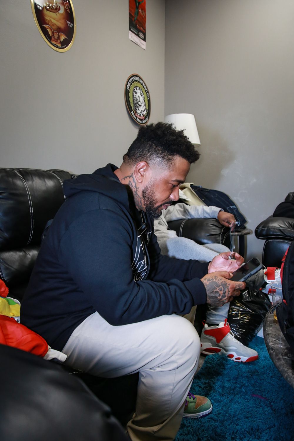 Someone in a navy hoodie sits on a leather couch while looking down at their phone in a living room setting.