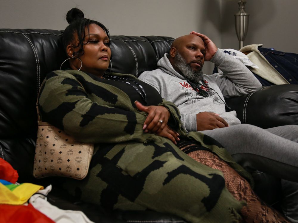 Two people relax on a leather couch, one wearing camouflage and the other in casual grey attire.