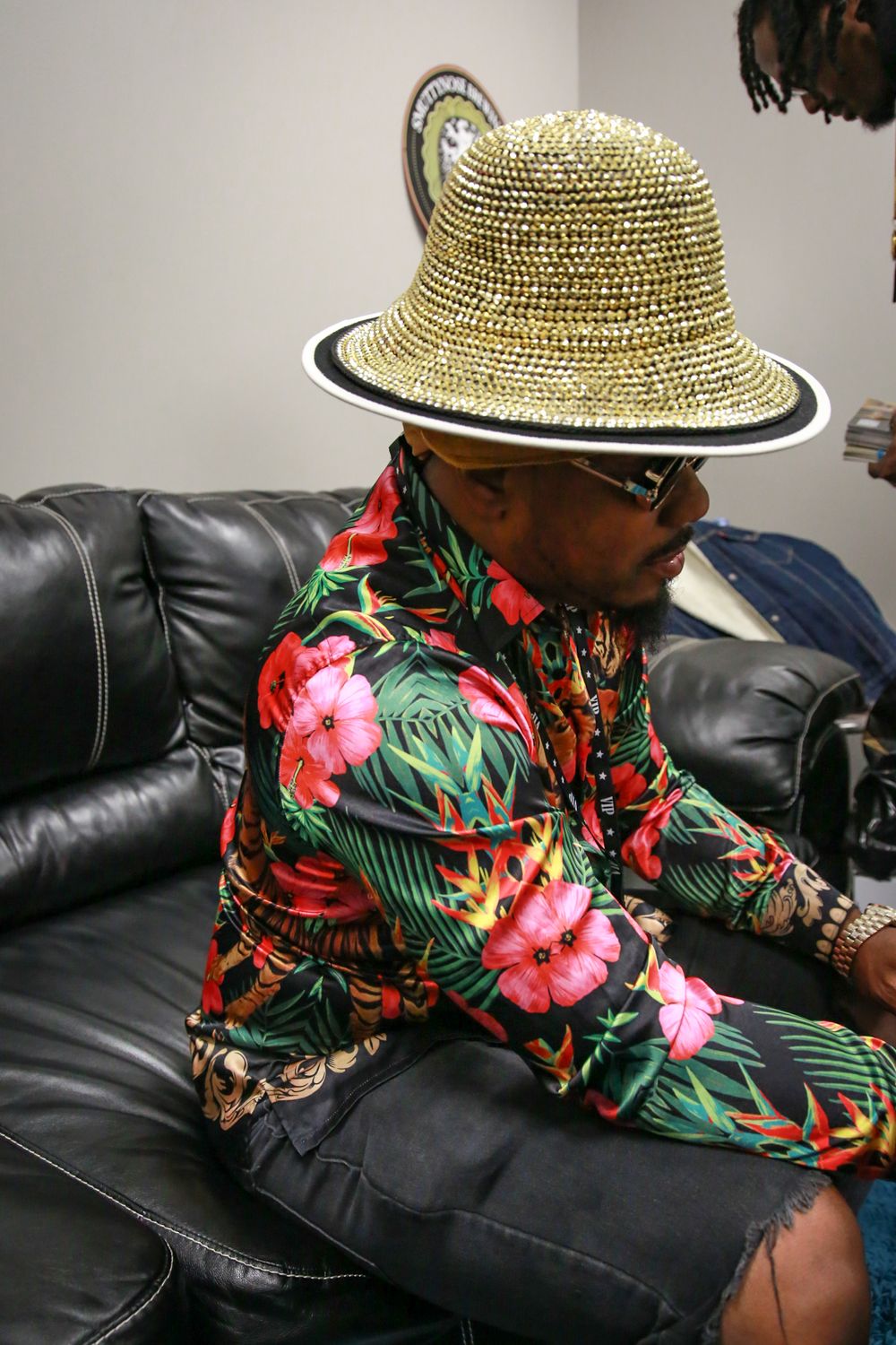 Person relaxing on leather couch wearing tropical floral shirt and straw hat with black trim.