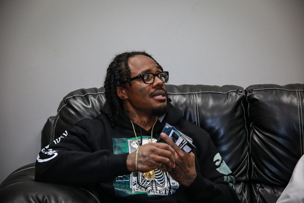 Someone wearing glasses and a black Raiders sweatshirt laughs while relaxing on a leather couch.