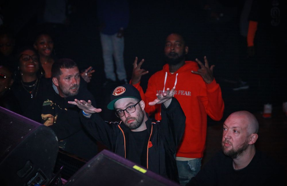 People gather at a dimly lit event, posing and making gestures while a photographer captures the moment.
