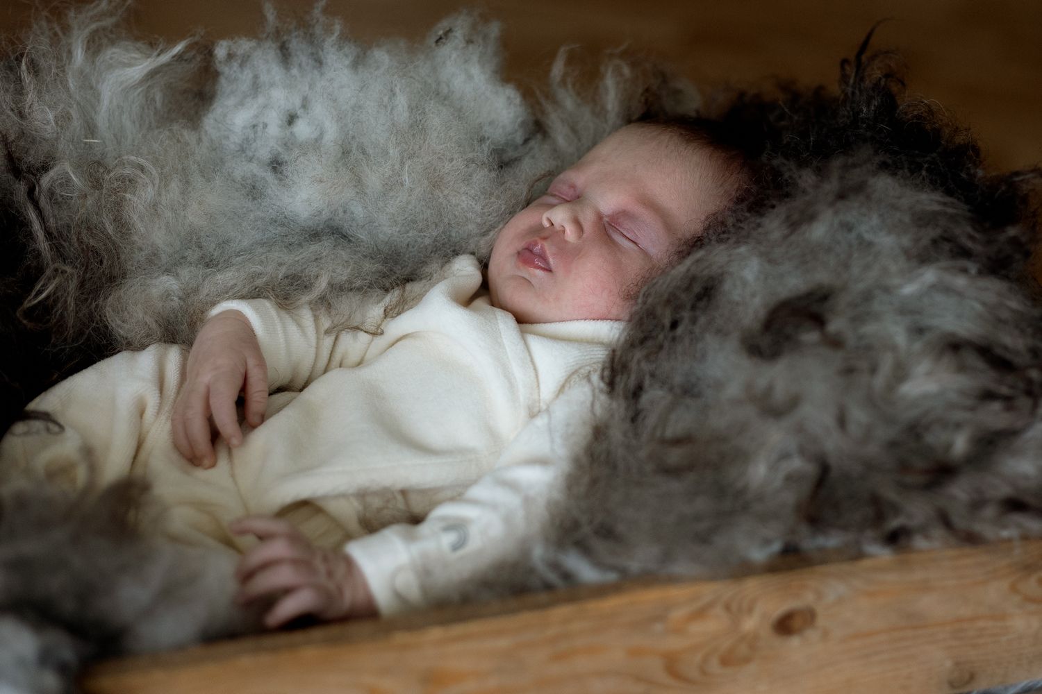 Artistic series showing sleeping baby surrounded by feathers on wooden surface.