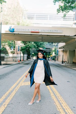 Graduate in white dress and academic regalia poses on campus at Georgia State University.