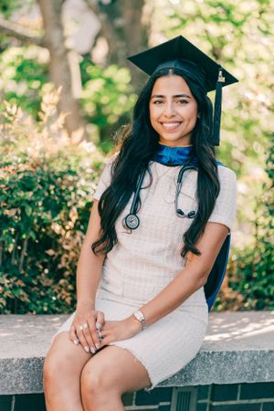 Graduate in white dress and cap poses outdoors for graduation photos.