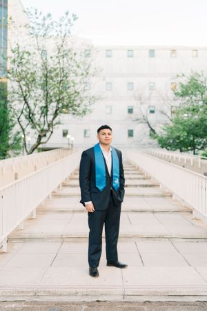 Young man in a suit with a blue graduation stole stands confidently on a bridge at GSU graduation