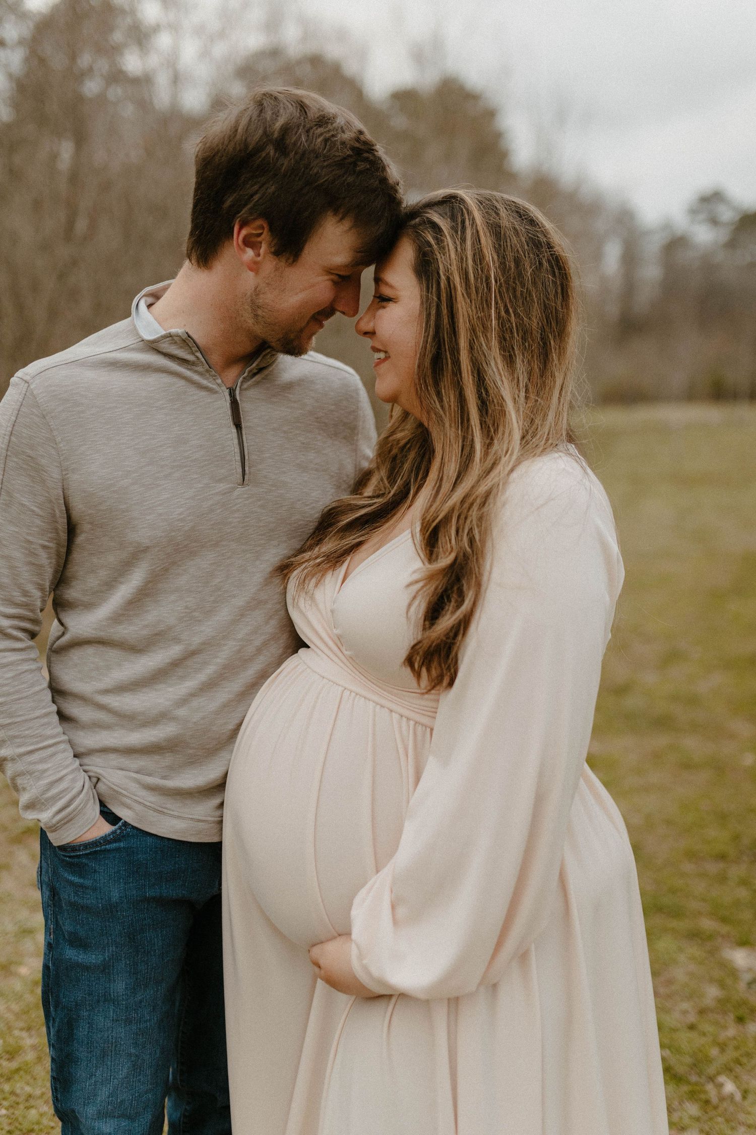 Intimate outdoor maternity portrait of couple in cream and grey clothing sharing tender moment.