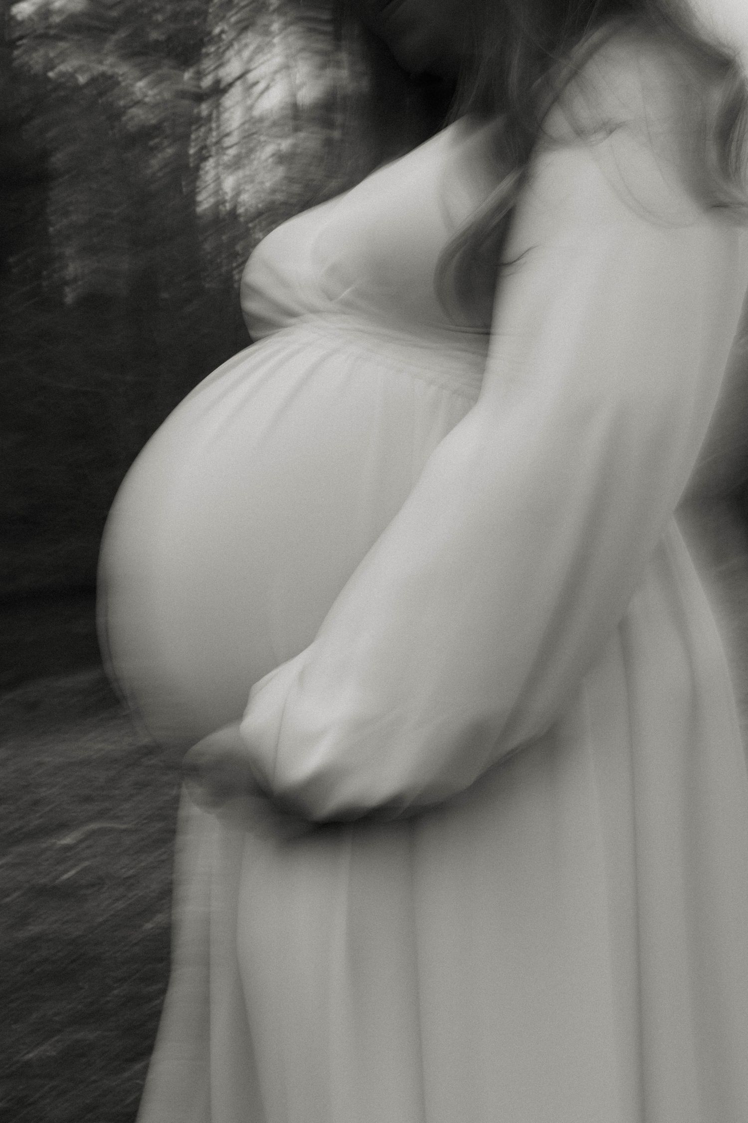 Artistic black and white profile shot of pregnant woman's belly in flowing dress.