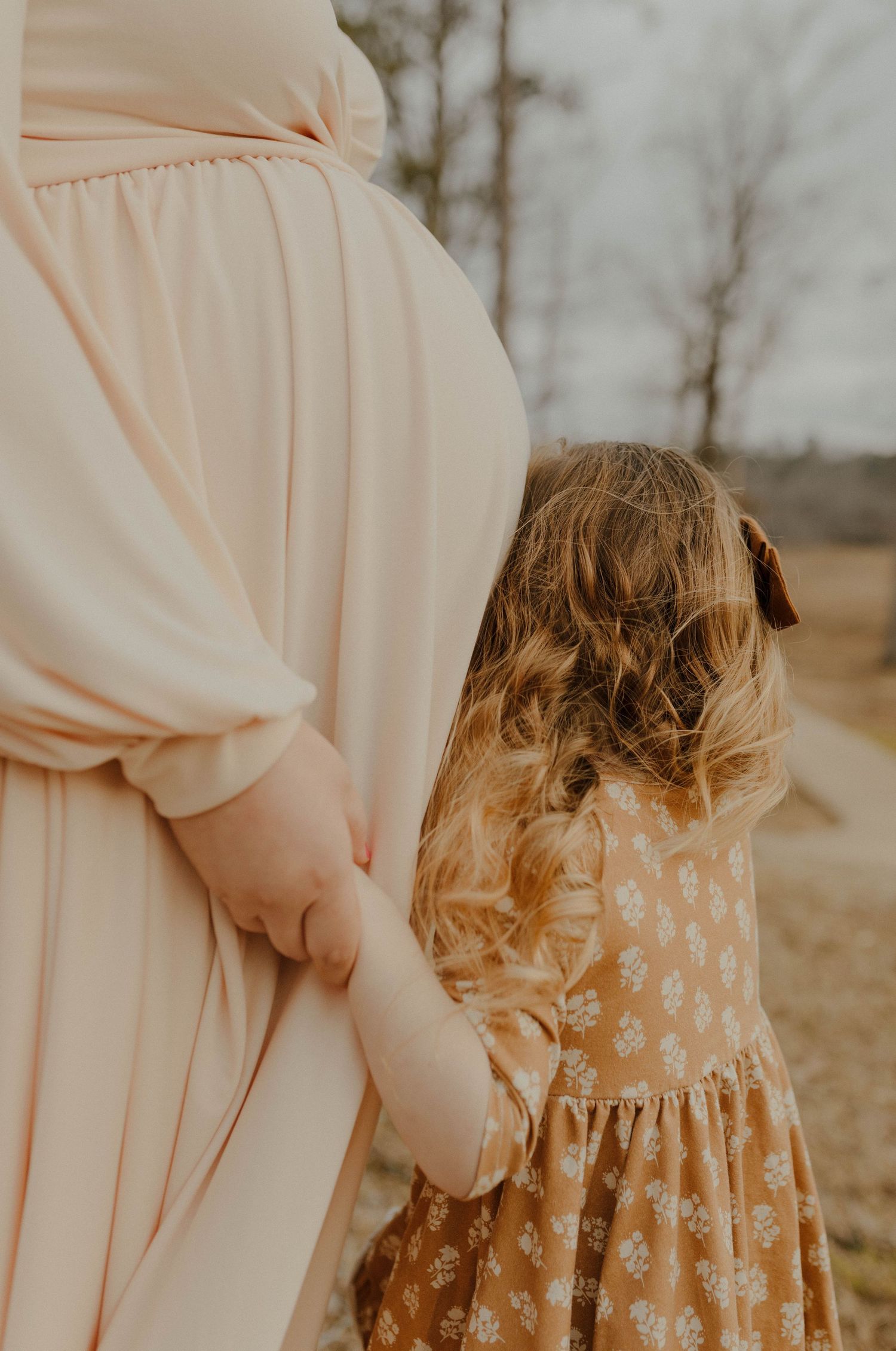 Close-up of pregnant belly in cream dress with small child in floral dress standing beside.