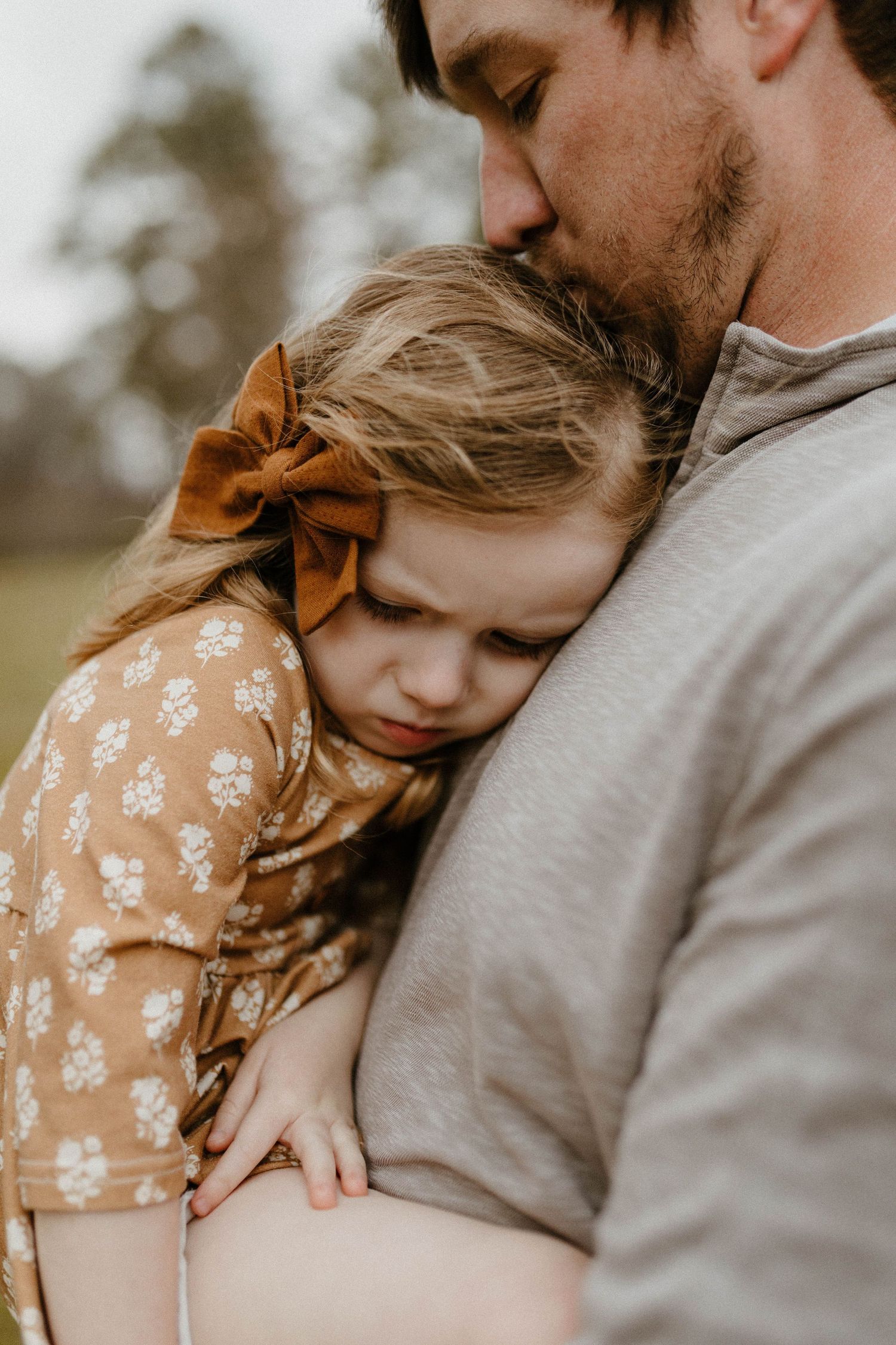 Tender moment between parent in grey sweater and small child wearing floral dress with bow.