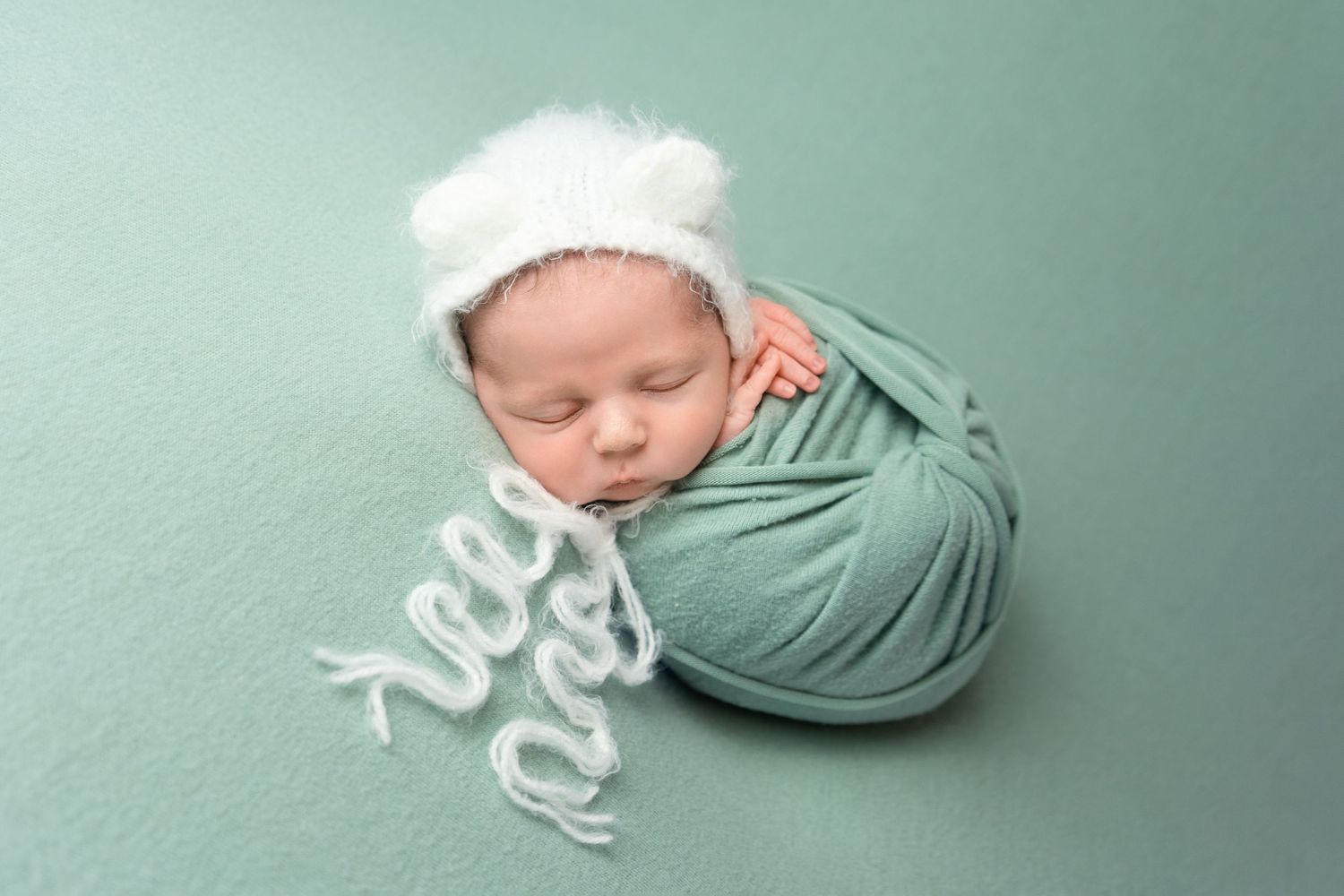 Newborn baby boy wrapped in a sage green blanket, with hands peeking out,  at newborn photoshoot in Doncaster.