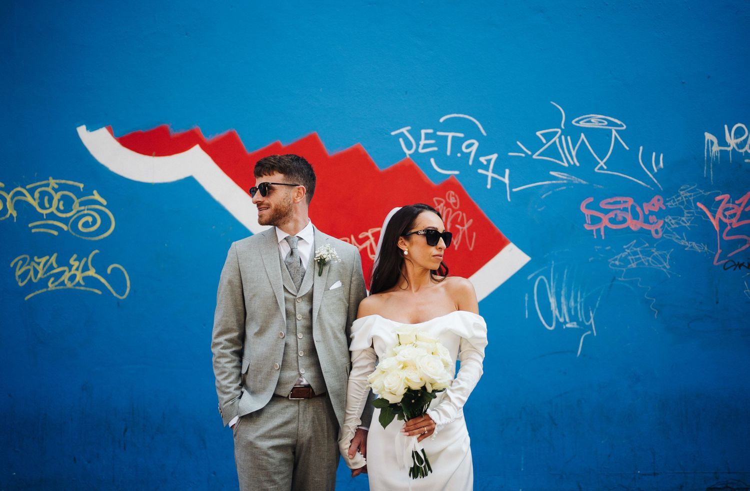 A stylish couple poses against a vibrant blue wall with red graffiti art details.