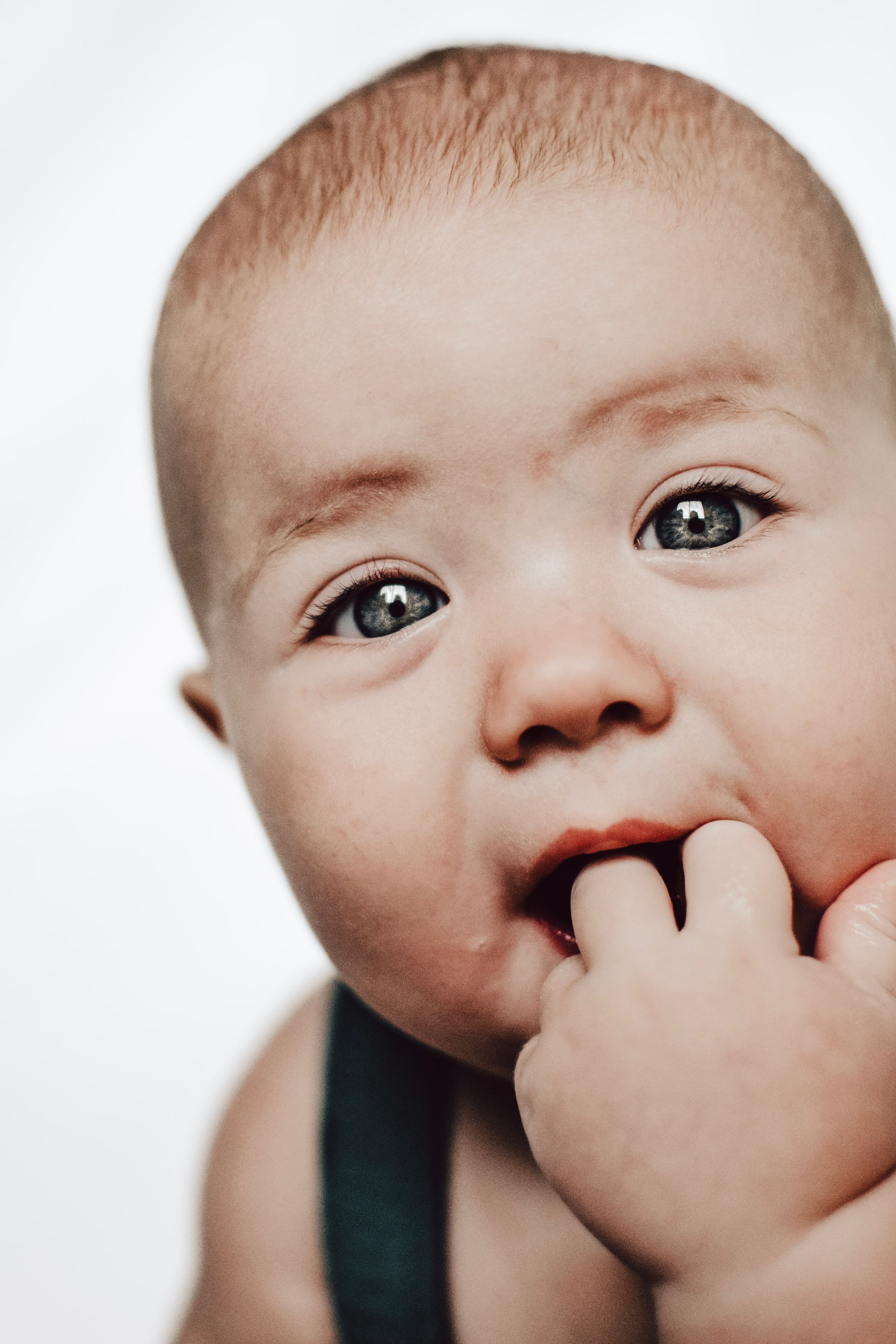 Close-up of baby with bright eyes sucking thumb against white background.