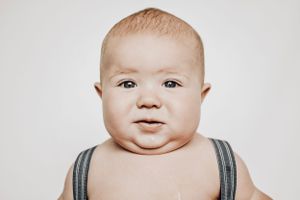 Portrait of a chubby baby wearing striped suspenders against neutral background.