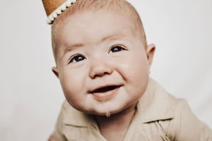 A joyful baby wearing a light colored collared shirt smiles at the camera.