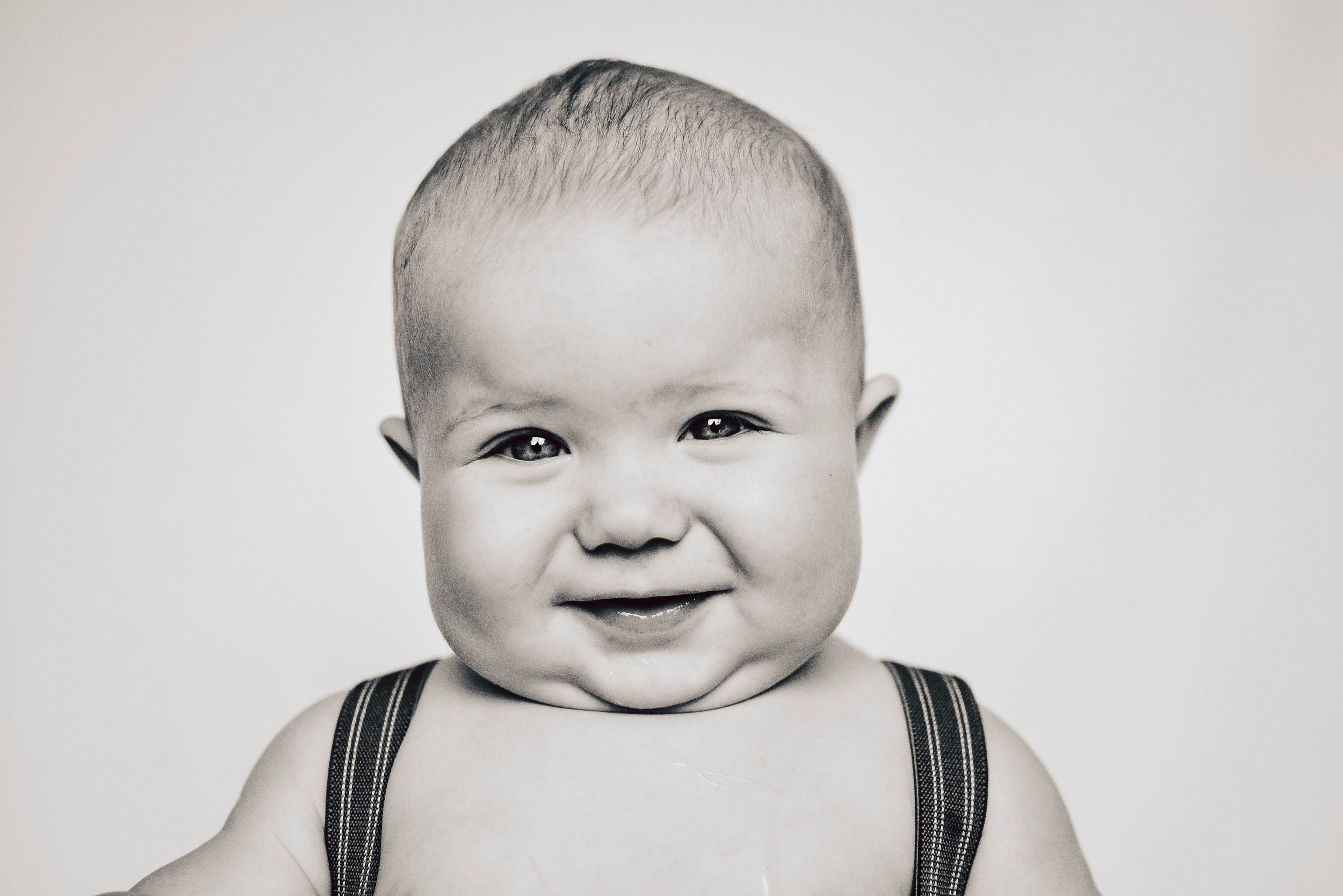 Smiling baby in black straps against white background in black and white portrait.
