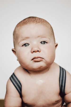 Candid portrait of an infant with rosy cheeks wearing dark suspenders.