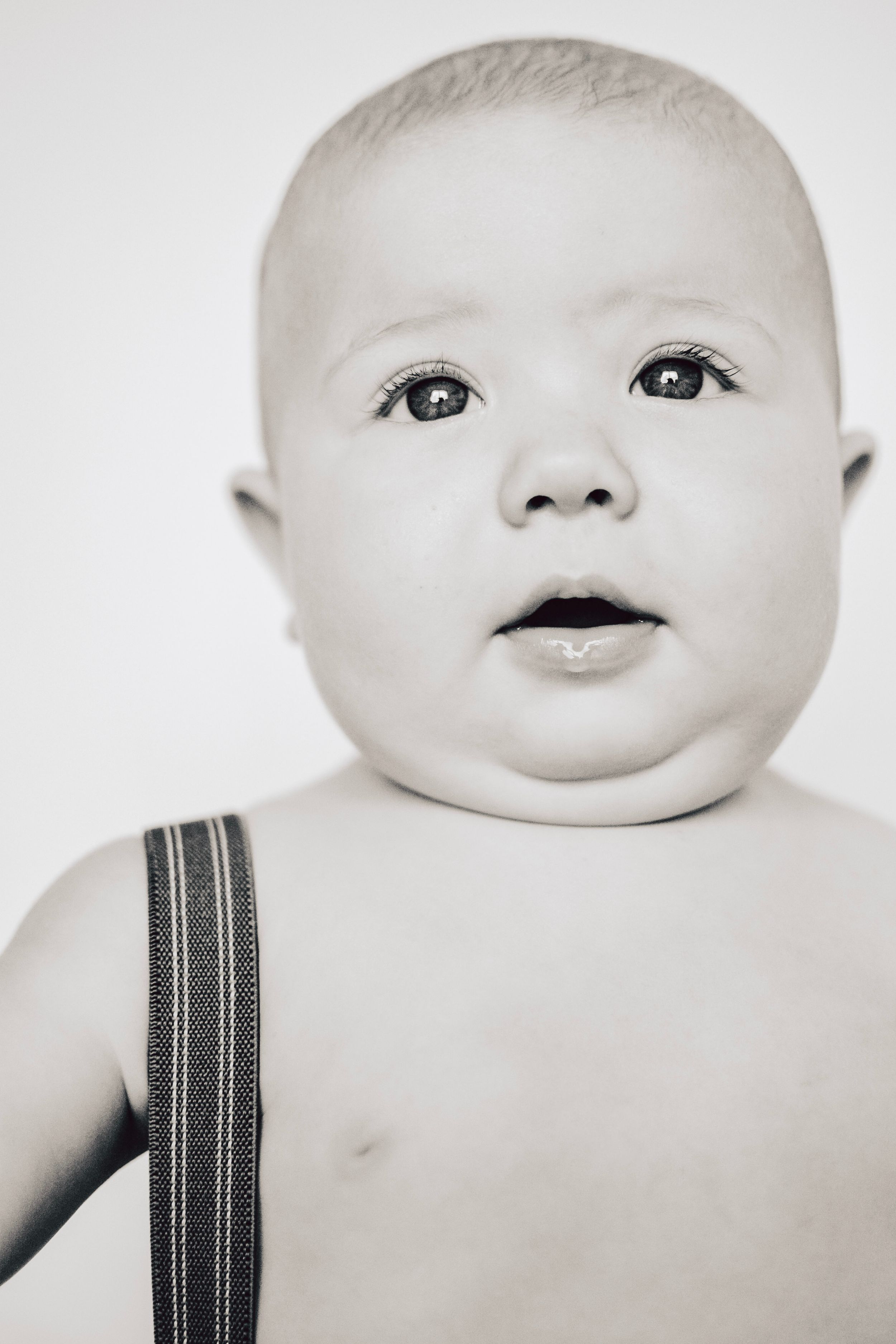 Black and white studio portrait of an infant wearing suspenders.