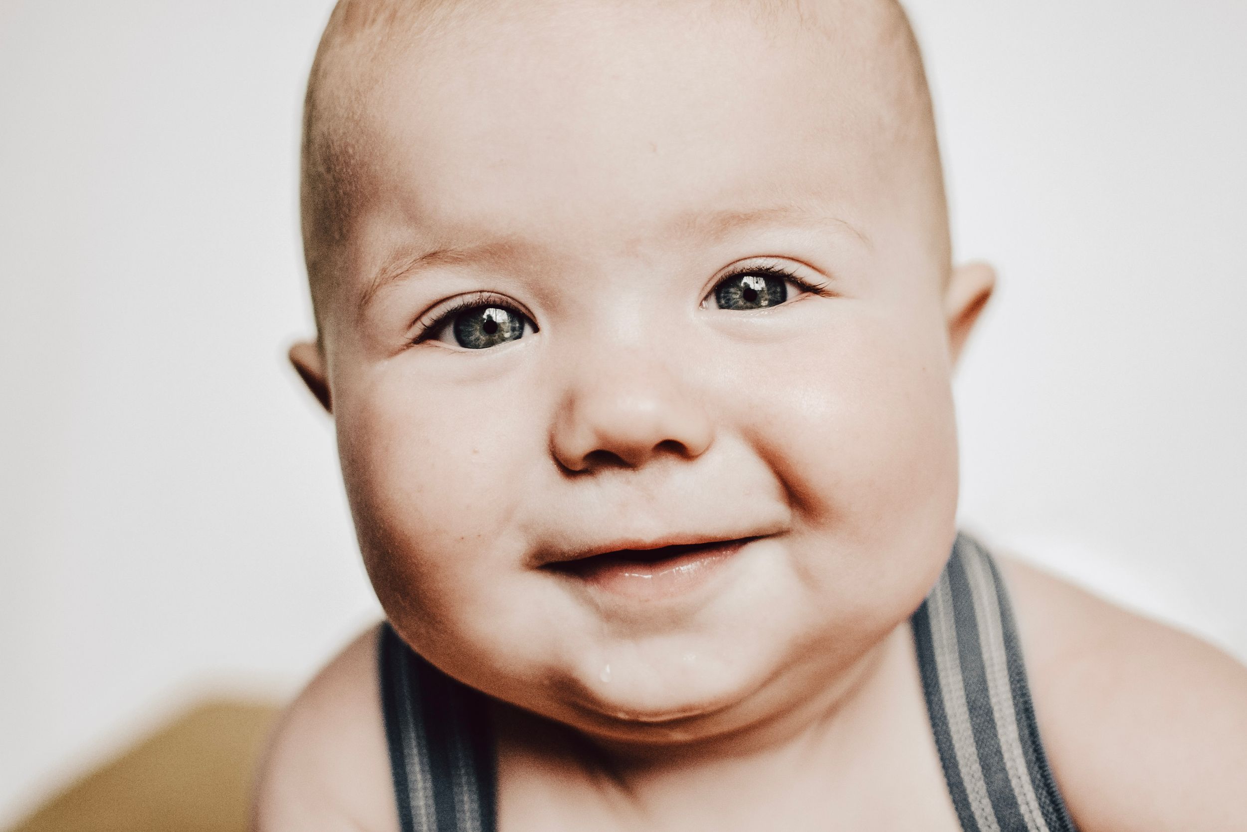 Close up portrait of a smiling baby wearing black striped straps against white background.
