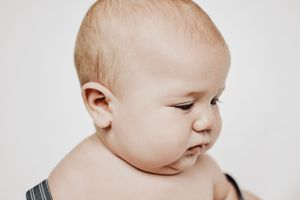 Studio portrait of an infant in black straps looking to the side against light background.