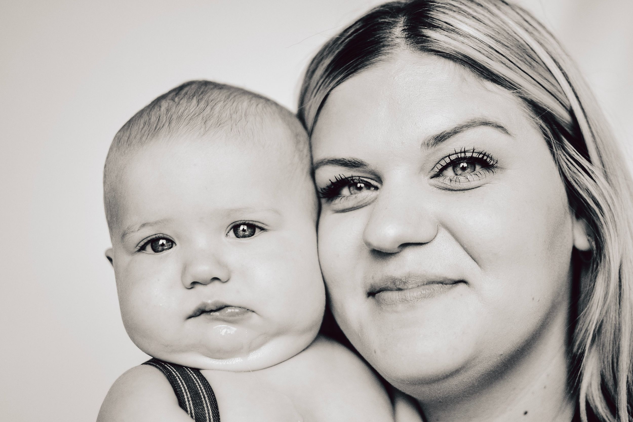 Black and white portrait of a parent and baby against neutral background.