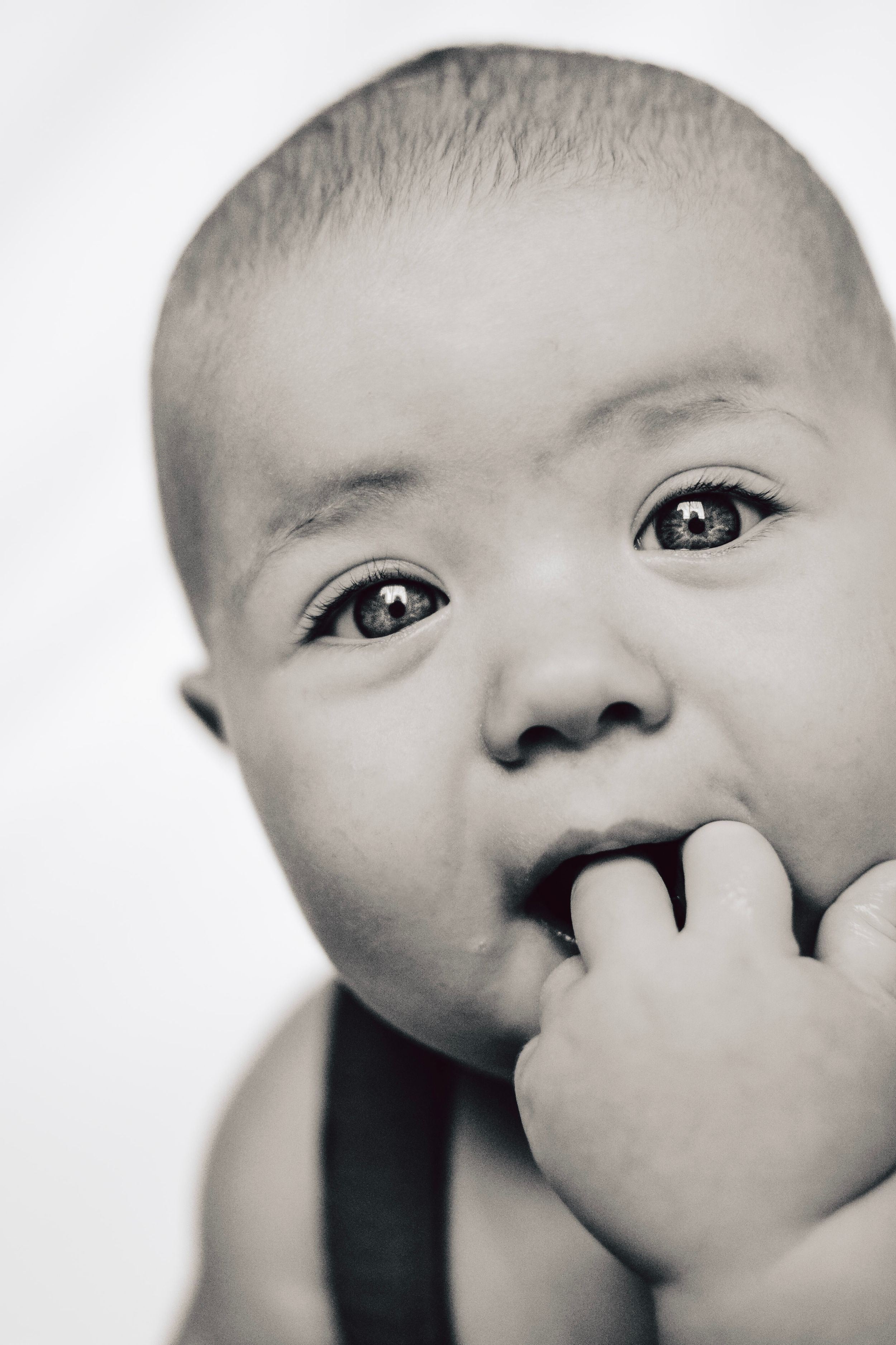 Black and white close-up of baby with finger in mouth wearing suspenders.