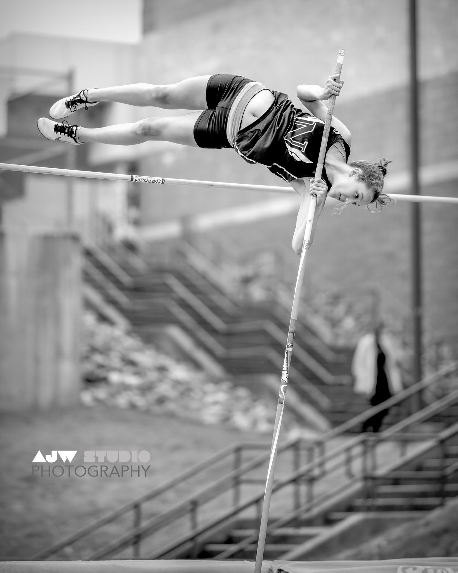 Black and white photo of pole vaulter clearing bar in mid-jump.