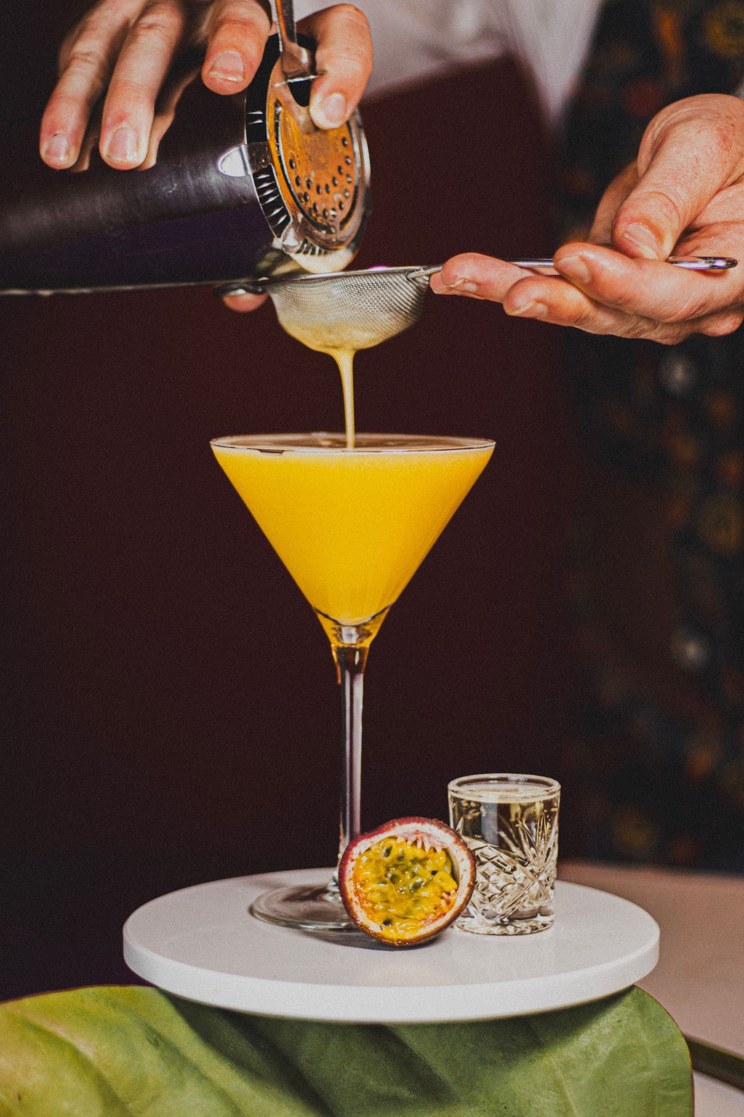 Afwerking van een Pornstar Martini met prosecco shot, passievrucht en zeefje voor de perfecte cocktail.