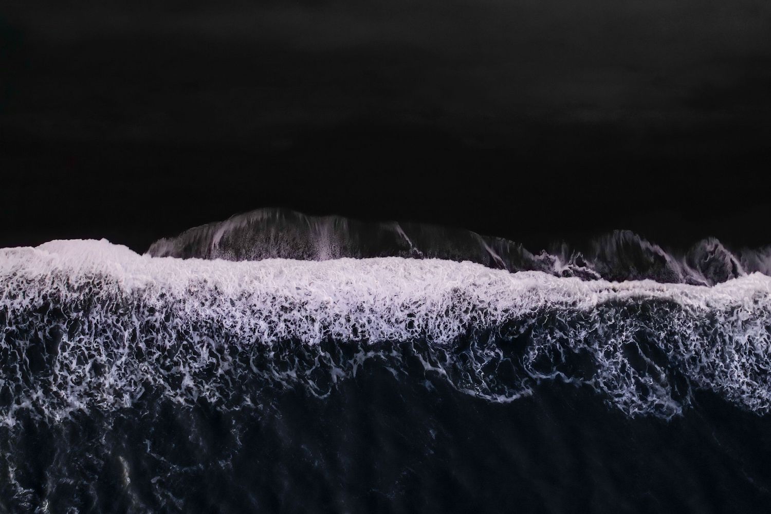 Dark ocean waves creating dramatic patterns in black and white photography.