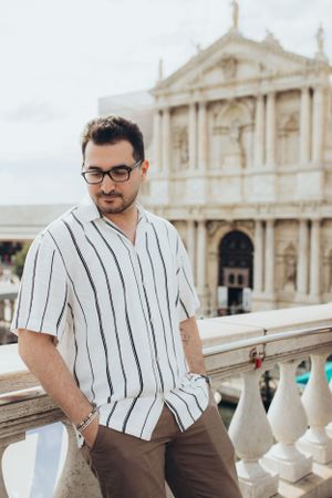 Person in striped shirt poses against classical architecture backdrop.