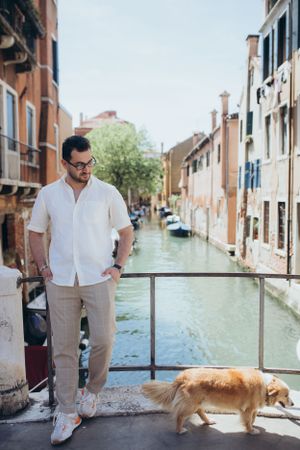 Person with dog on Venice bridge overlooking picturesque canal with colorful buildings.