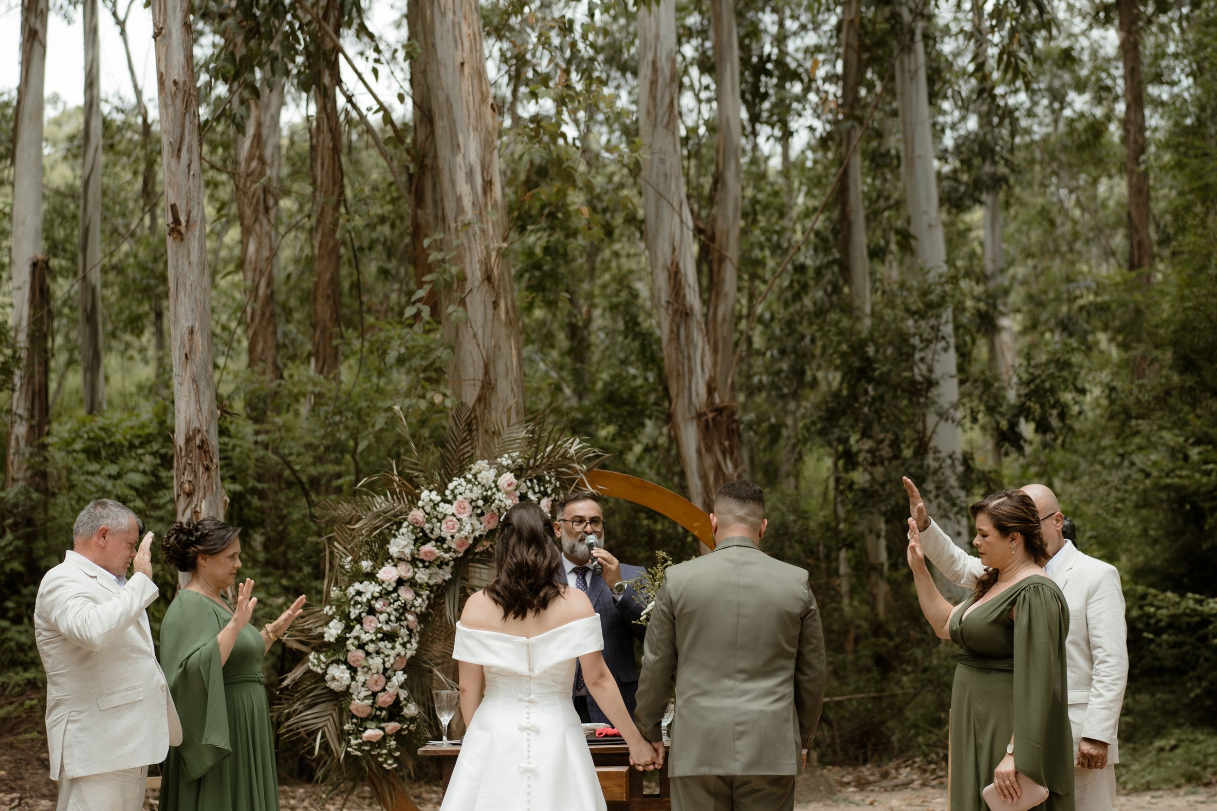Wide shot of wedding ceremony in eucalyptus forest with wooden arch.