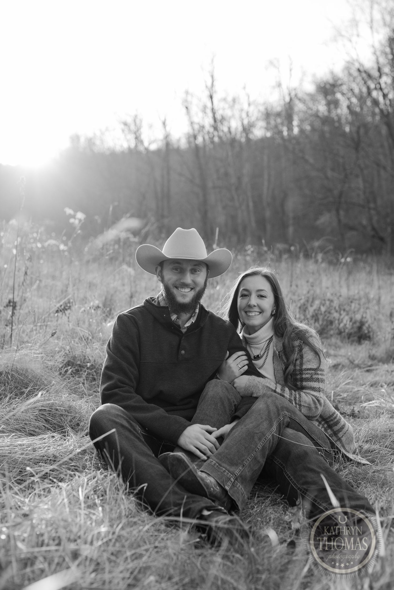 A black and white portrait of a couple sitting together in a fall meadow.