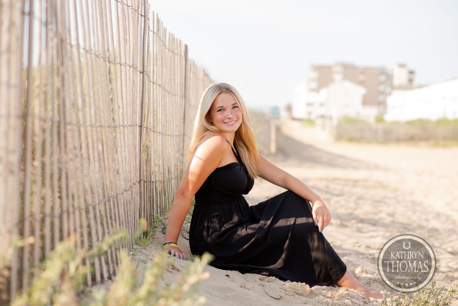 Portrait by wooden beach fence during golden hour wearing black dress.