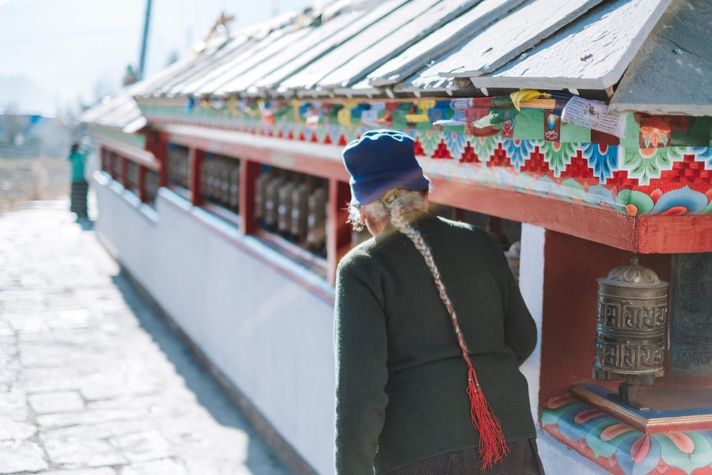 A collection of prayer wheels with colorful decorative patterns line up along a temple wall in Nepal.