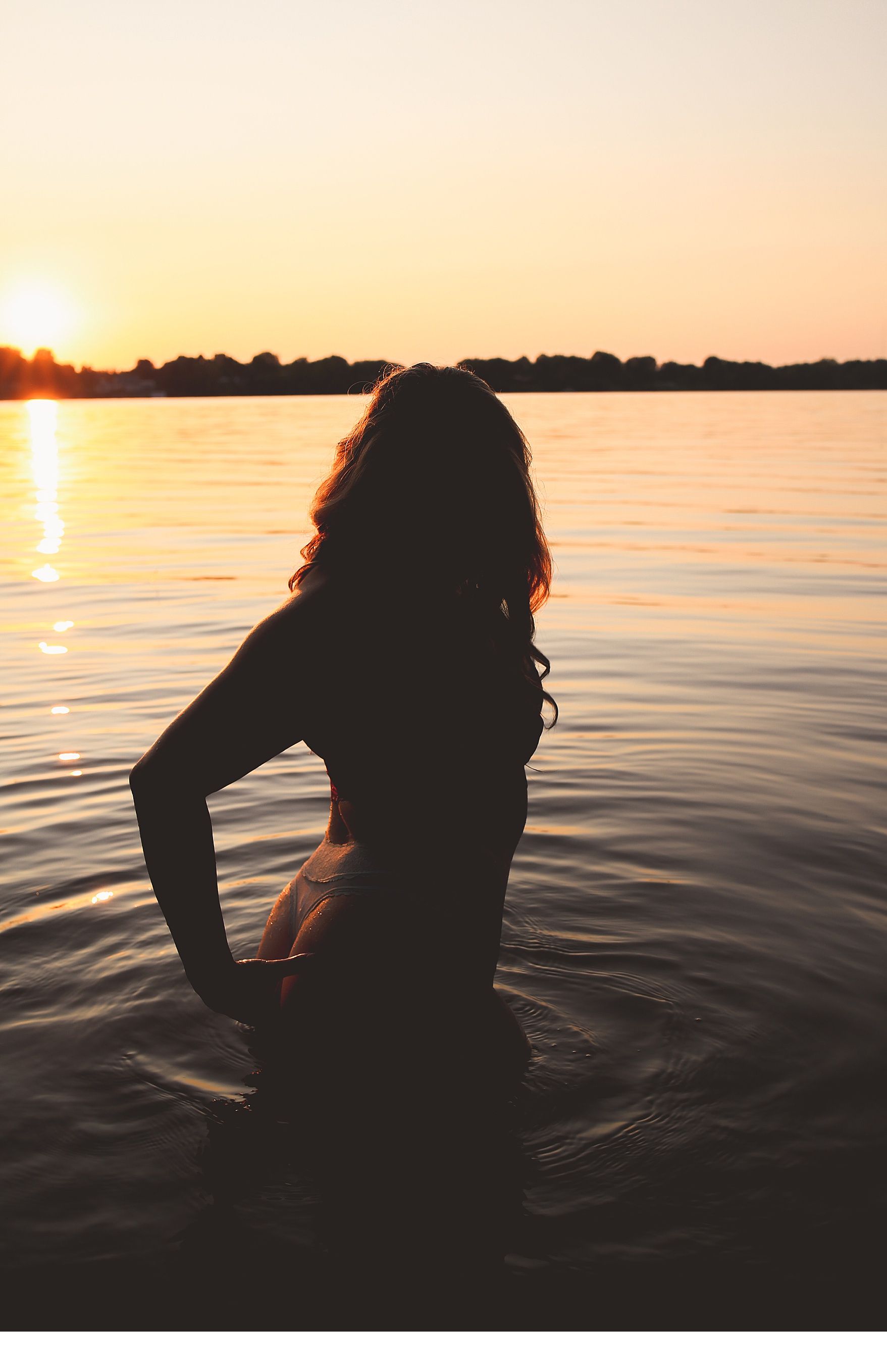 Silhouetted figure in water during golden sunset creating dramatic reflection on rippling lake surface.