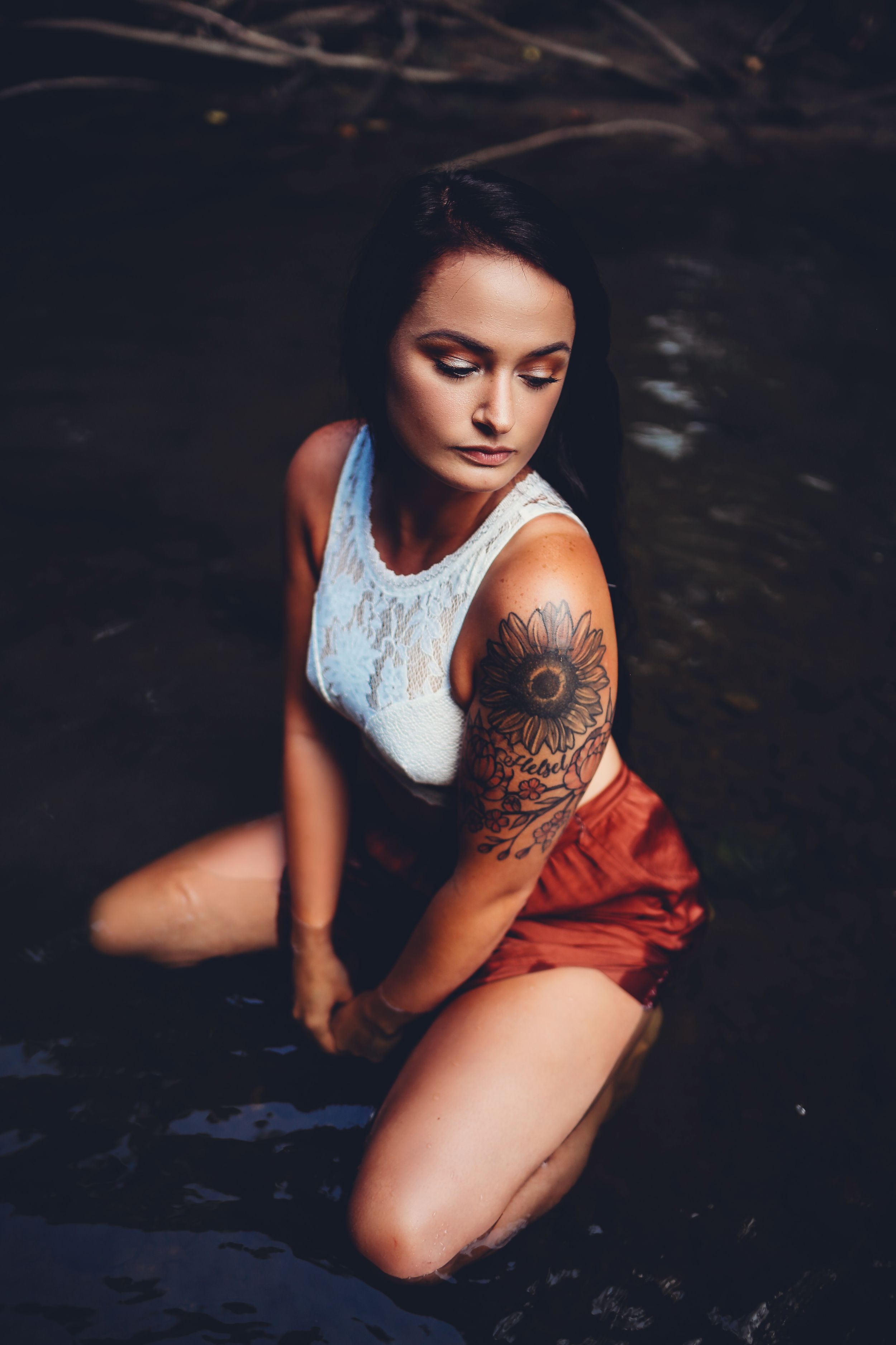 Woman in white tank top with visible tattoos poses in dark water setting.