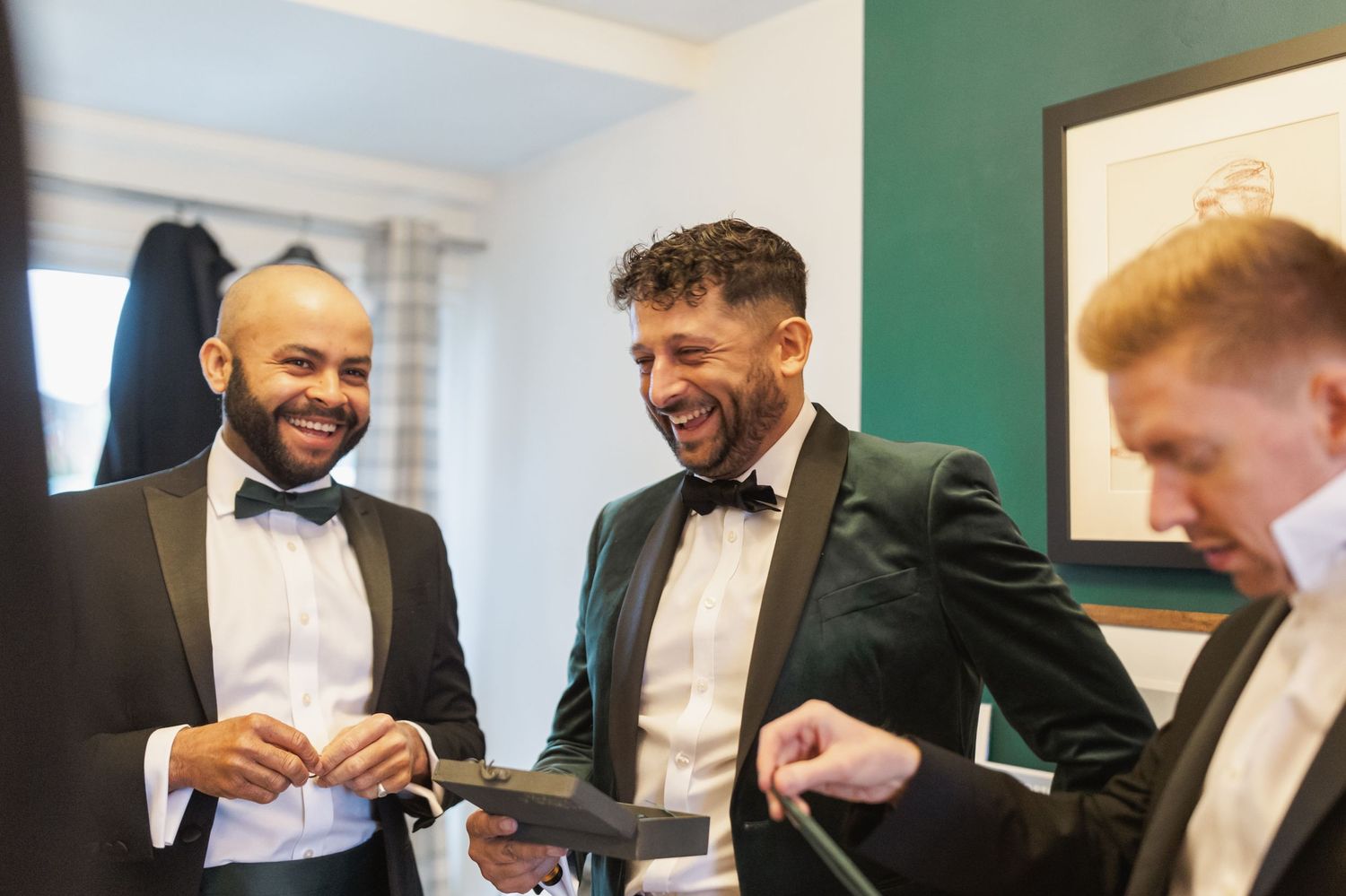 Groomsmen in formal black tuxedos and bowties sharing a laugh together.