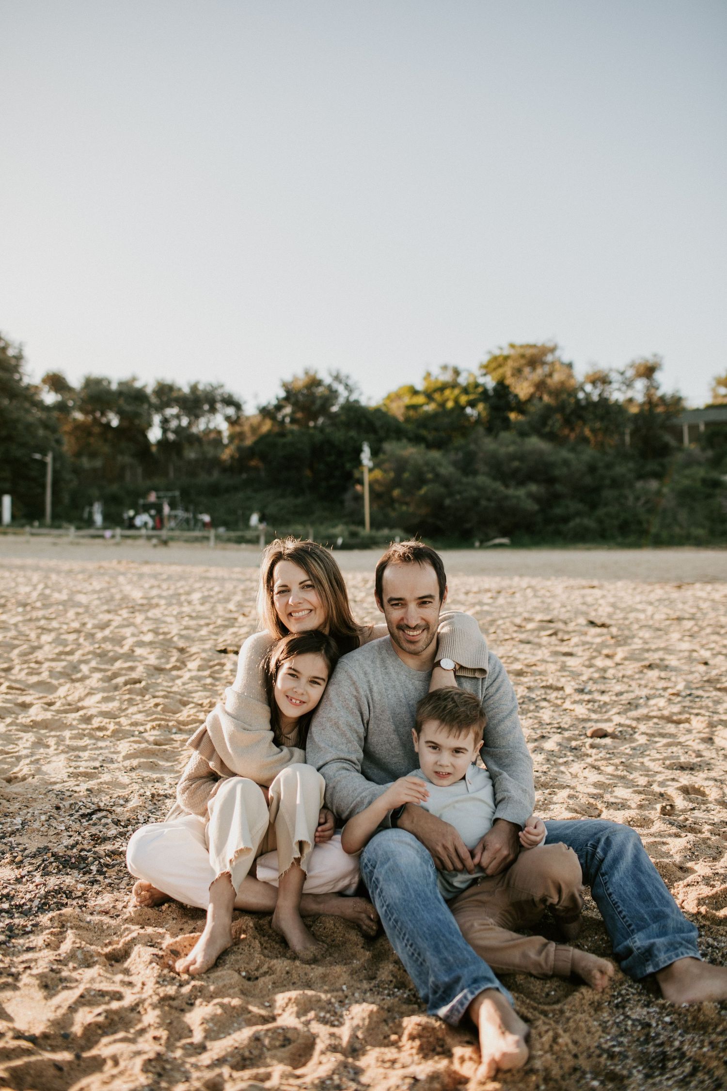 Happy family of four sitting together on sandy beach in warm golden sunset light.
