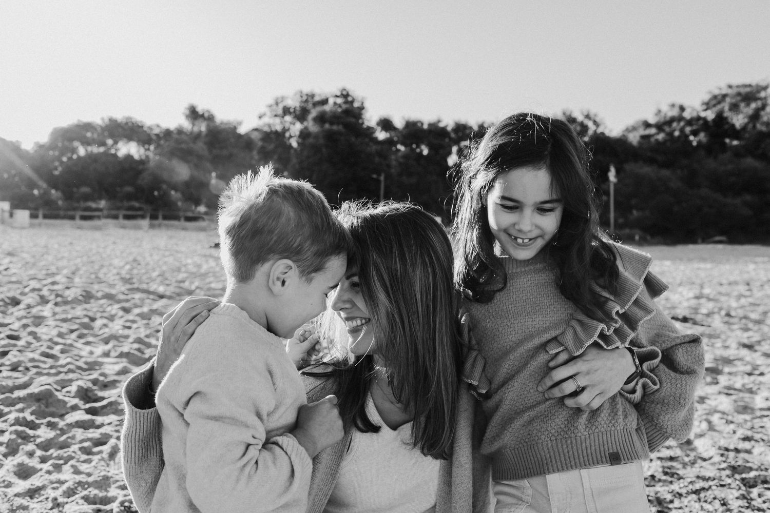 Black and white photo of two children hugging their mother on a beach.