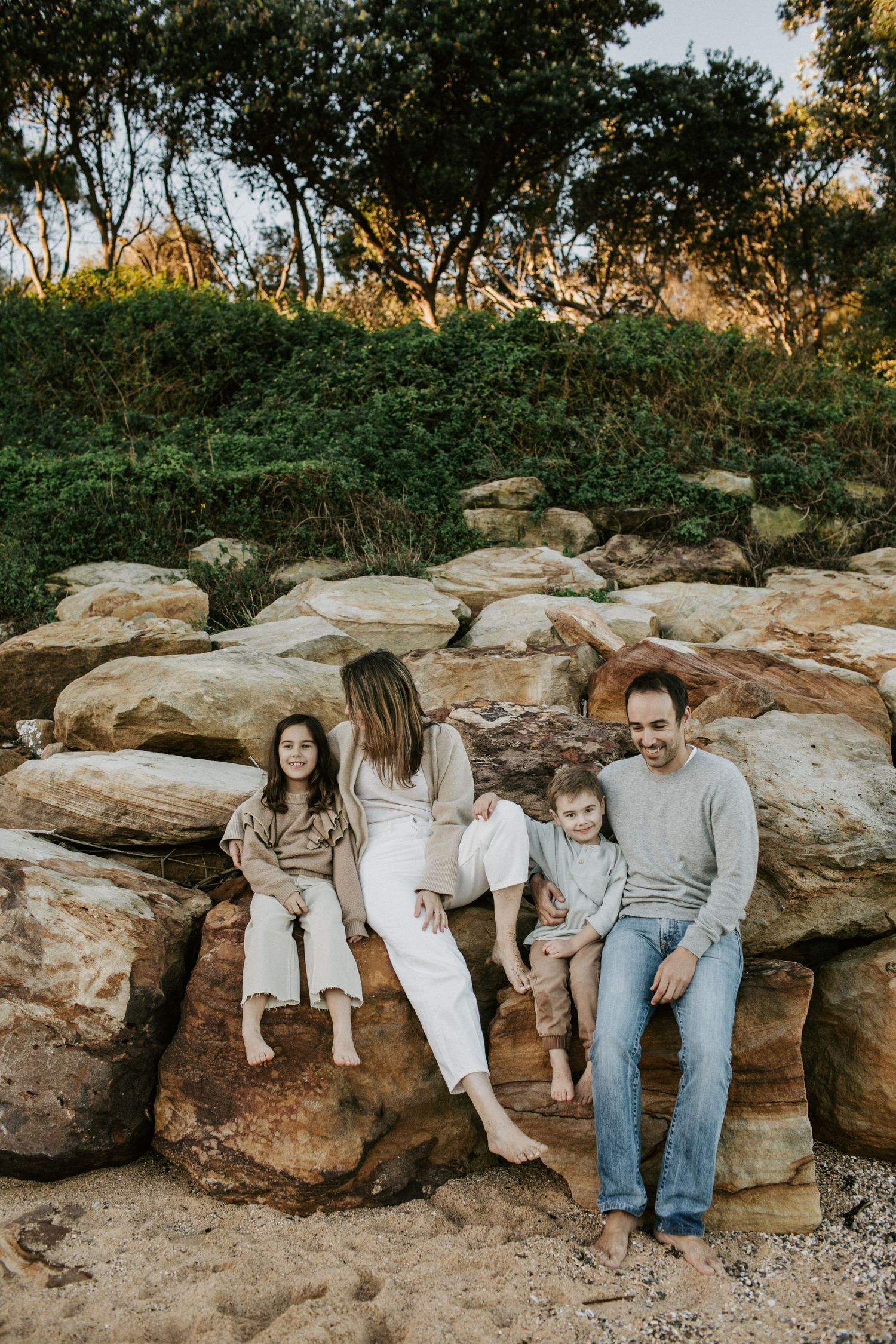Family of four relaxing and laughing together on large sandstone rocks near a beach.