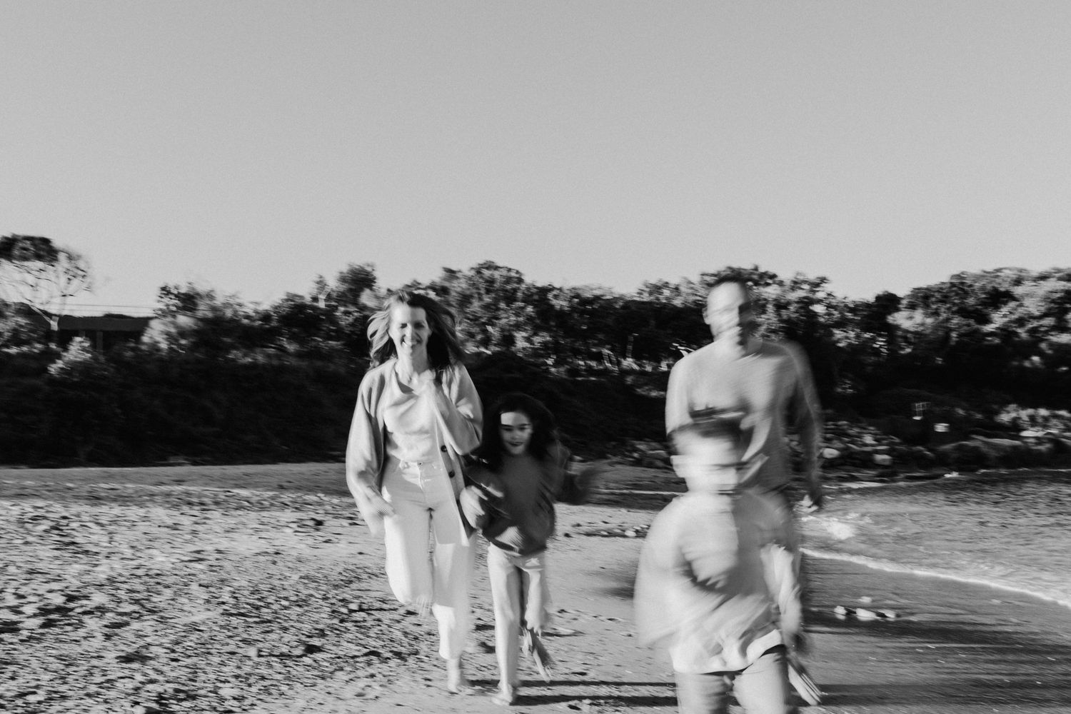 Black and white photo of a family walking along a sandy beach near the water's edge.