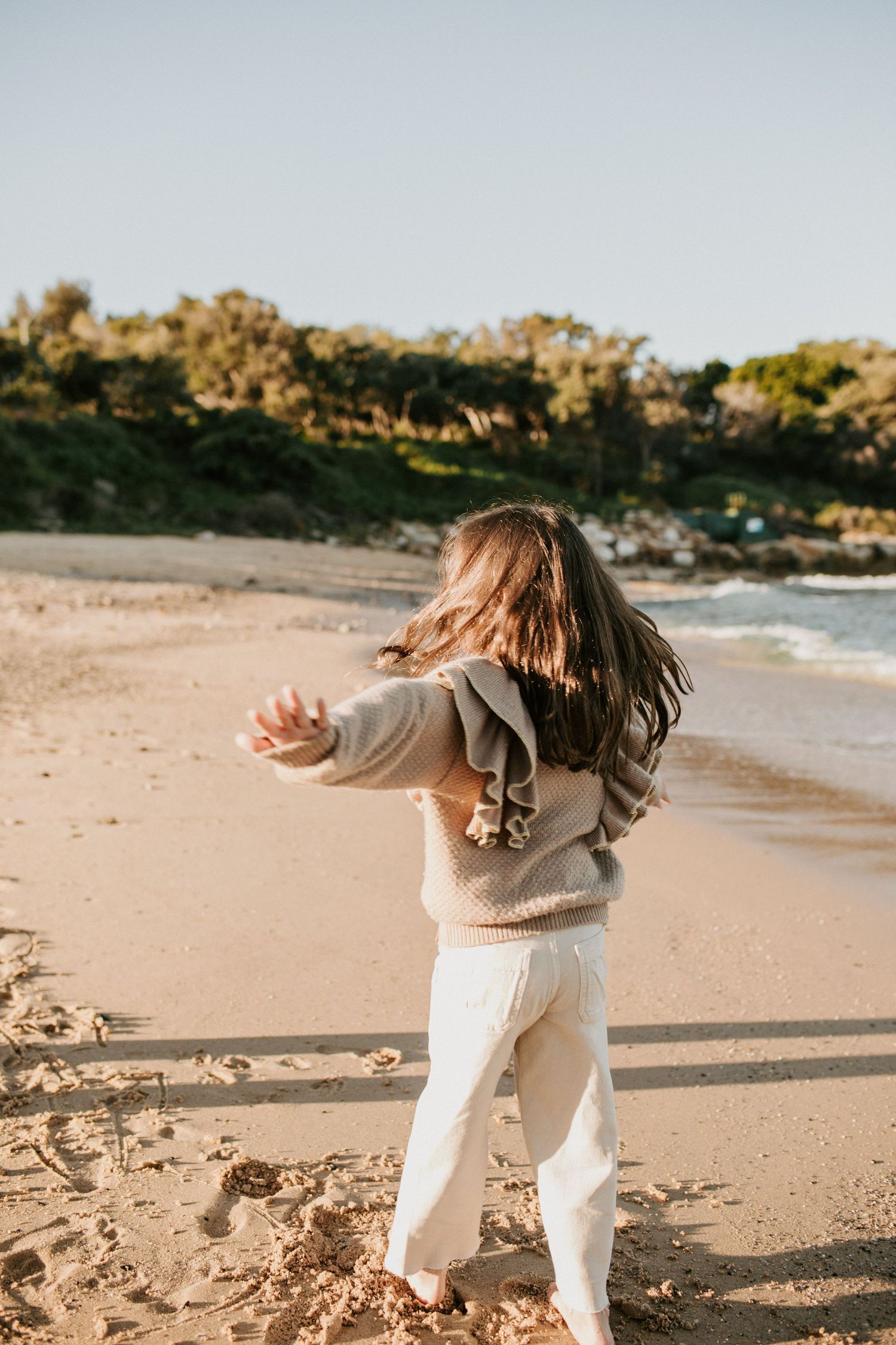 Young girl spinning with arms outstretched on a sunny sandy beach.